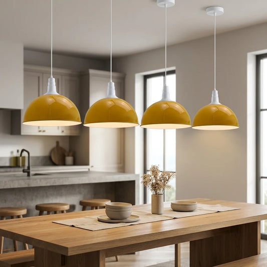 Four modern pendant lights with glossy mustard yellow dome shades and white cord suspensions, hanging over a wooden dining table in a bright, contemporary kitchen.