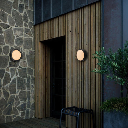 LED round bulkhead wall lights installed on modern wooden and stone exterior near entrance, emitting warm ambient light – available at Ledsone.