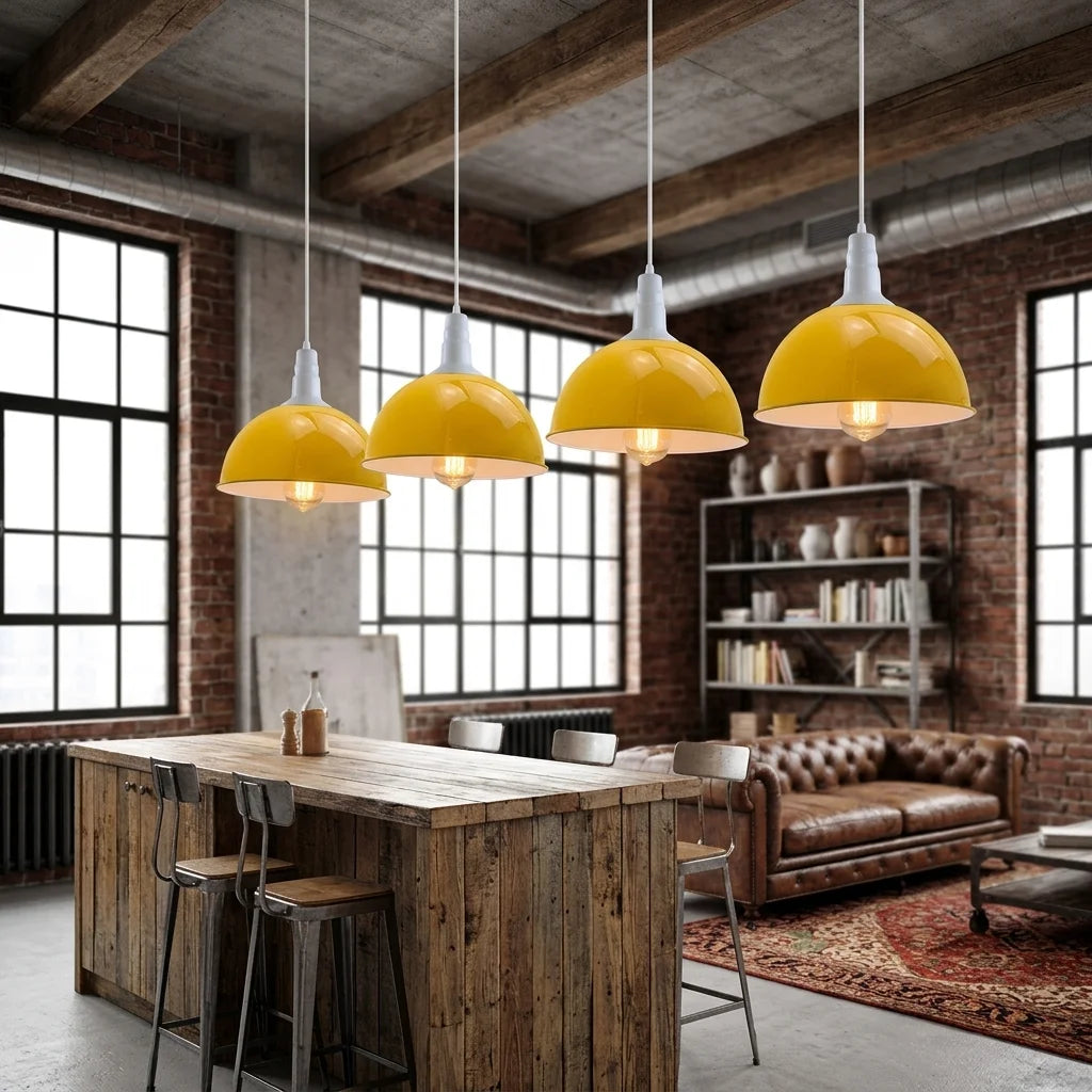 Four yellow dome pendant lights hanging over a rustic wooden dining table in a loft-style room with brick walls, large windows, and a leather sofa.