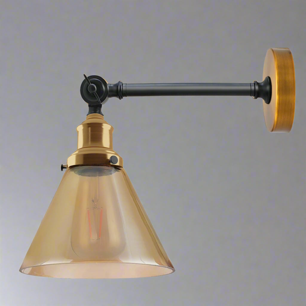  A fancy living room wall light featuring an adjustable dark grey arm, brass accents, and a clear, amber-tinted conical glass shade with a vintage-style bulb, mounted on a plain grey wall.