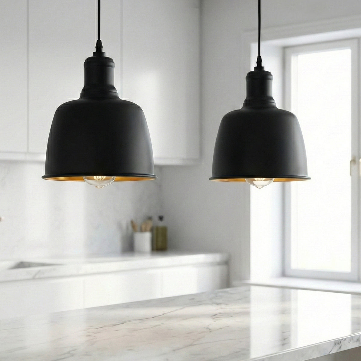 Two matte black pendant lights with a warm gold interior lining hang over a modern white marble kitchen island in a bright, contemporary kitchen.