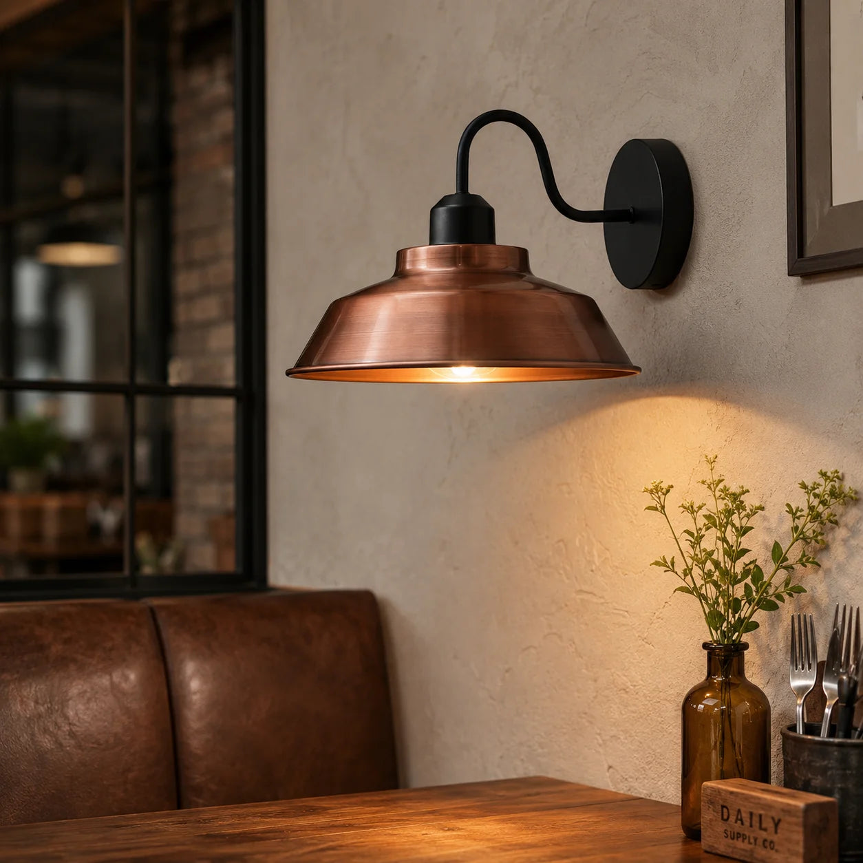 Copper wall sconce lighting a cozy corner with a brown leather sofa and wooden table.