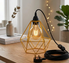 Geometric gold lamp with a lit bulb on a wooden surface, surrounded by decor items.