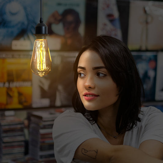 Warm illuminated Edison filament pendant lamp hanging beside a dark-haired woman in a relaxed indoor setting