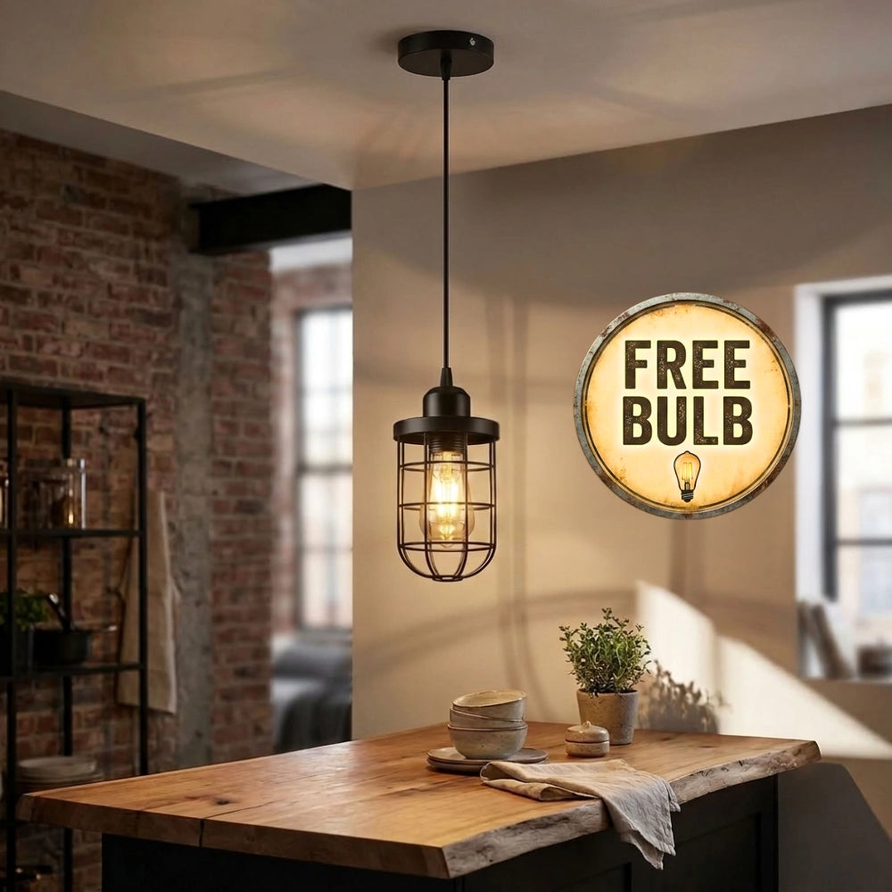 A black metal cage pendant light hanging in a modern loft-style room with a wooden table, brick wall, and a decorative circular 'FREE BULB' sign on the wall.