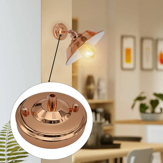 Rose gold metal ceiling rose base with a side screw fitting, shown in front of a warm lit wall light in a room
