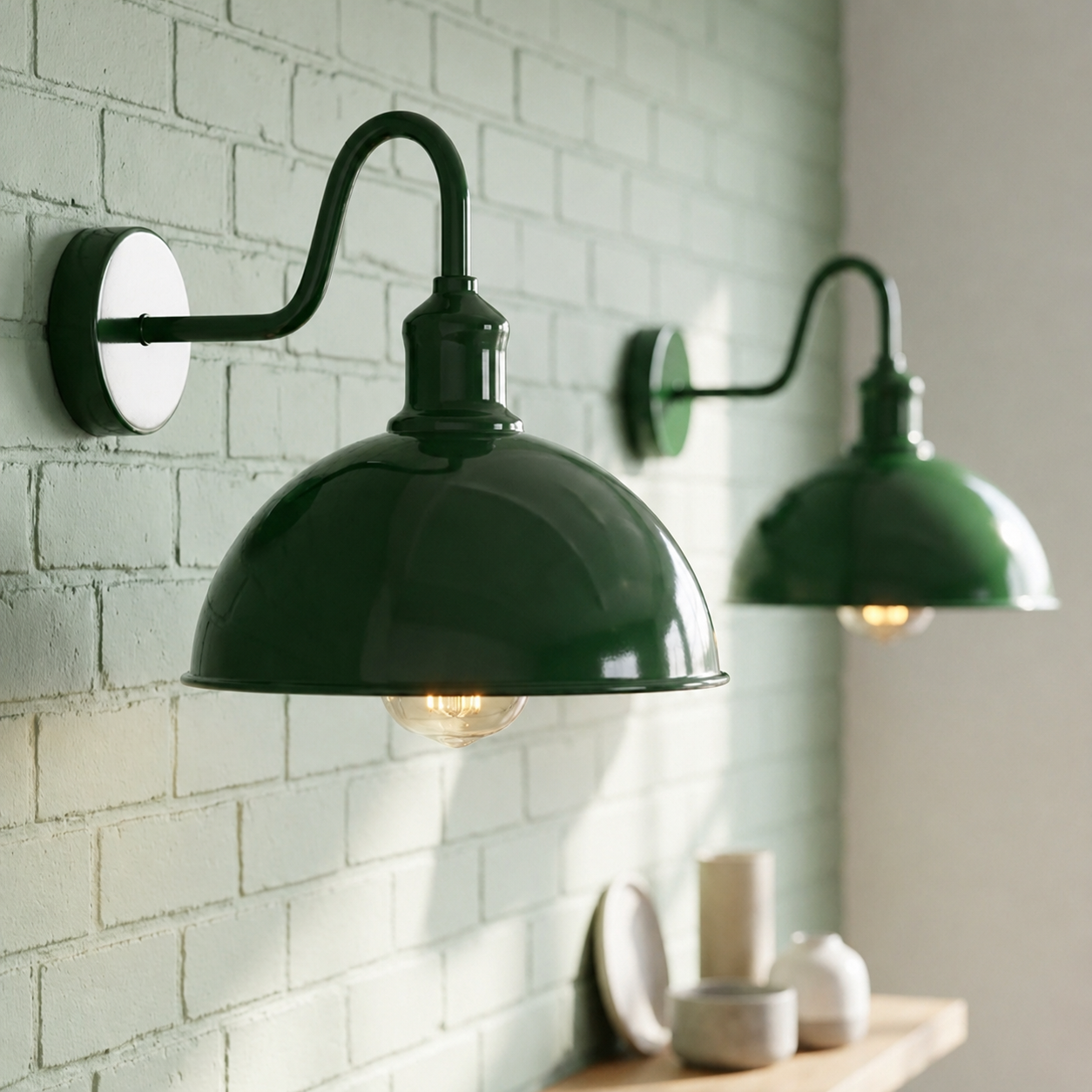 Two dark green industrial-style wall sconces mounted on a white brick wall, with one in sharp focus in the foreground and the other softly blurred in the background.