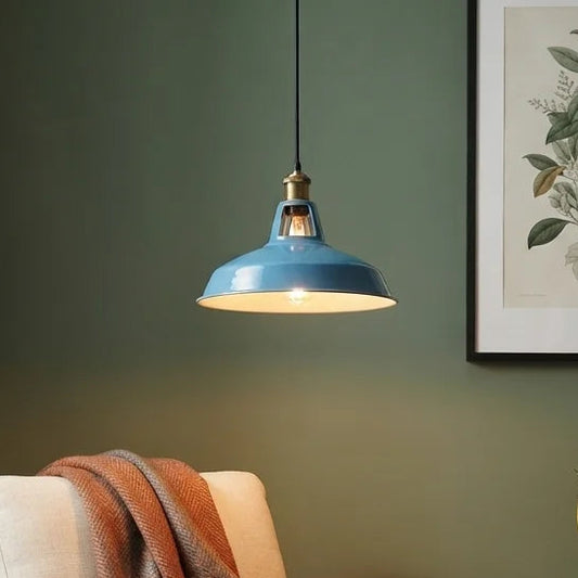 A mid-century modern armchair with cream upholstery and a dark wood frame, styled in a cozy room with a rust-orange and brown throw blanket, a blue pendant light, a small wooden side table with a plant, and a sage green wall.